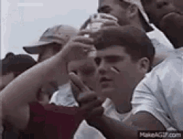a group of people are sitting in a stadium watching a game and one of them is giving the middle finger .