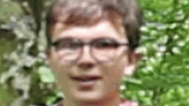 a blurry picture of a man wearing glasses standing in front of a tree .