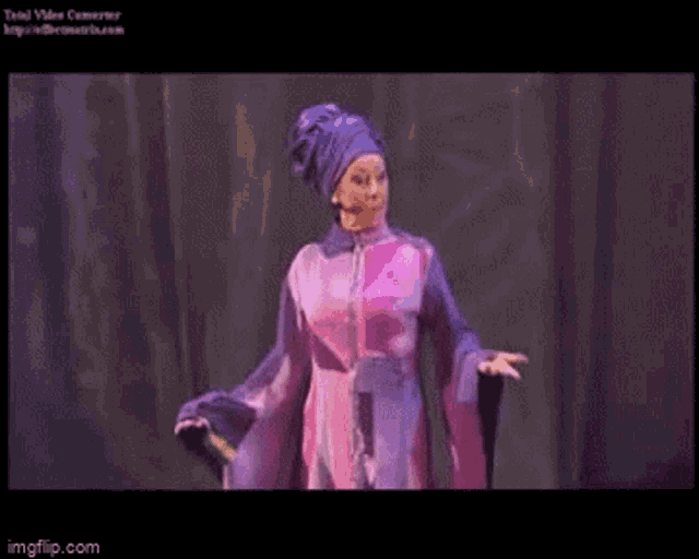 a woman in a purple dress and turban stands on a stage ..