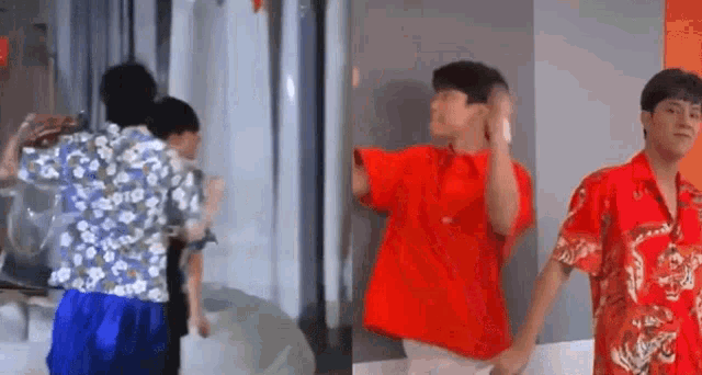 a group of young men are standing next to each other in a room . one of the men is wearing a red shirt .