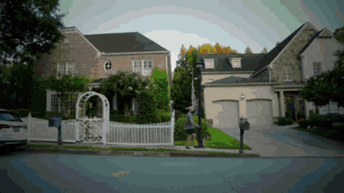a man walking in front of a house with a white fence