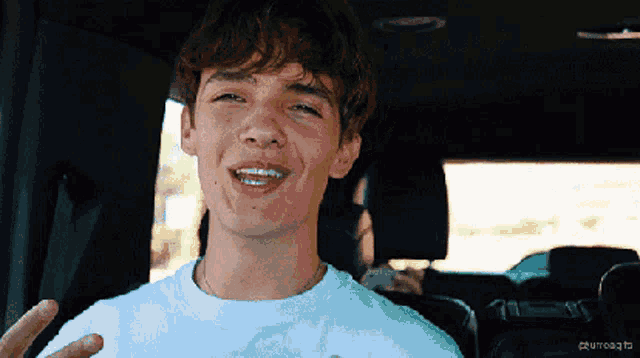 a young man in a white shirt is sitting in a car and smiling .