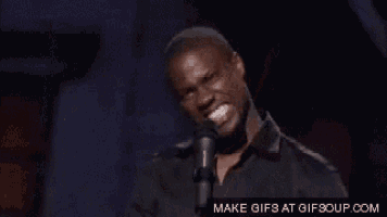 a man in a black shirt is speaking into a microphone and making a funny face .