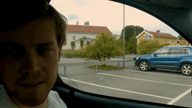 a man in a car looking out the window at a blue car parked in a parking lot