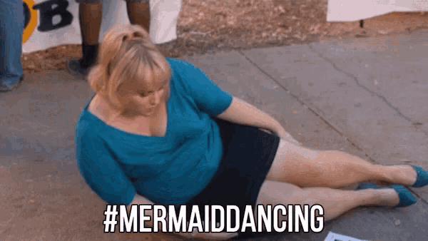 a woman in a blue shirt and black shorts is laying on the ground with her legs crossed and says #mermaiddancing .