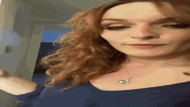 a woman with red hair is wearing a blue top and a necklace