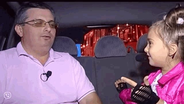 a man and a little girl are sitting in a car and the little girl is wearing a pink jacket