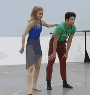 a man and a woman are dancing together in a dance studio . the woman is wearing a blue leotard .