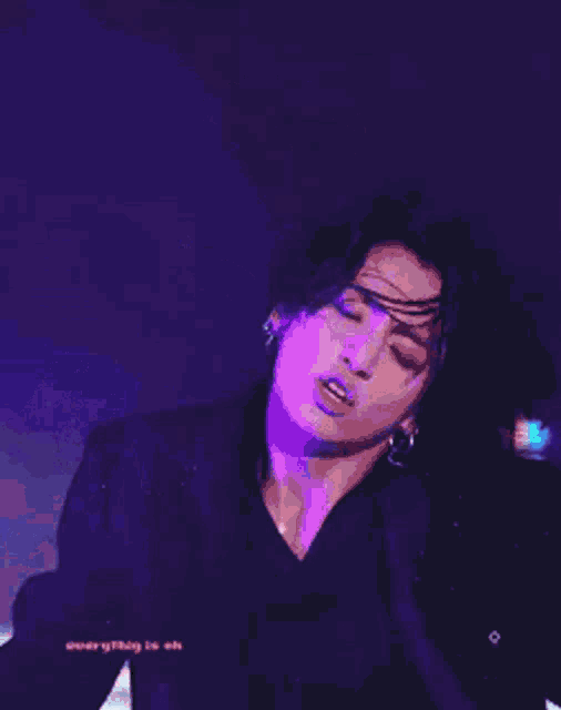 a young man in a black suit is standing in front of a purple background .