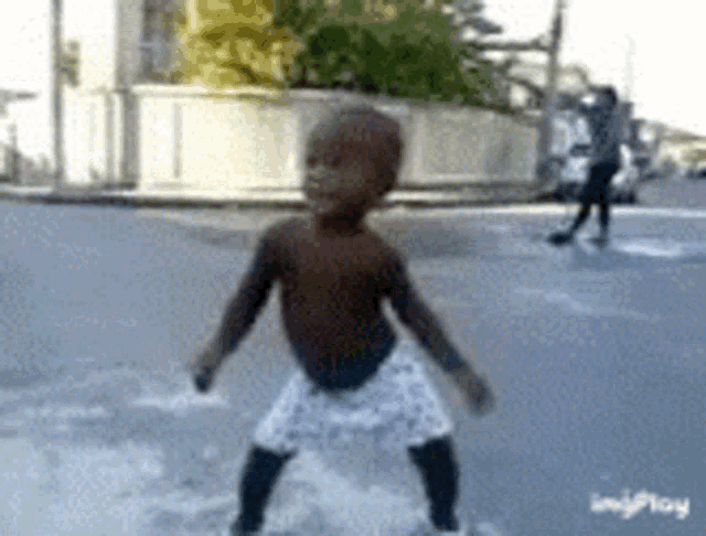 a little boy without a shirt is standing in the street .
