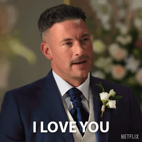 a man in a suit says i love you in front of flowers