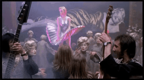 a man holding a guitar in front of a painting of a woman