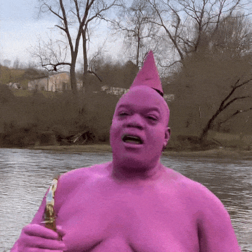 a man in a pink bodysuit is holding a bottle in front of a body of water