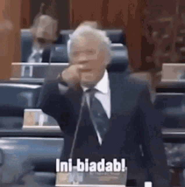 a man in a suit and tie is speaking into a microphone and says " ini biadabl " .