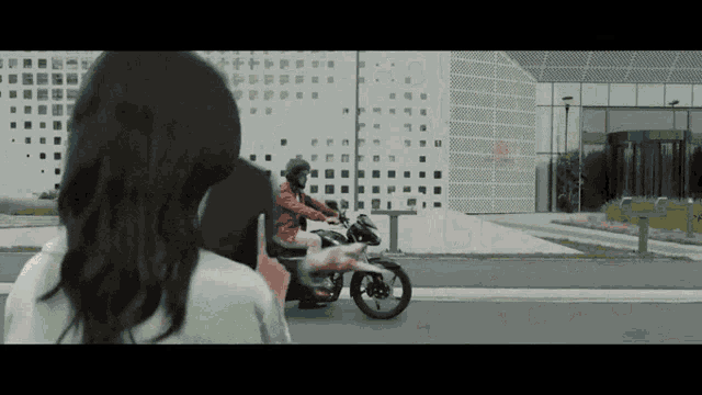 a woman is looking at a man riding a motorcycle on the street