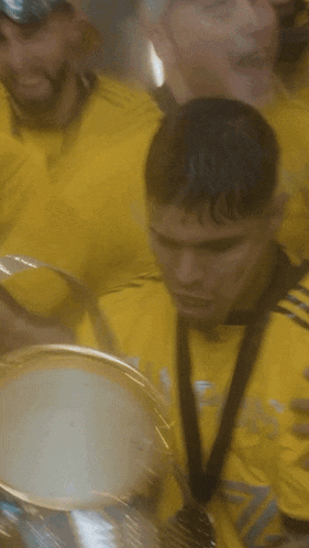 a man in a yellow adidas shirt is holding a trophy in front of his face