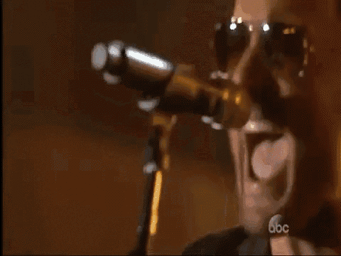 a man singing into a microphone while playing a guitar on a stage with abc in the background