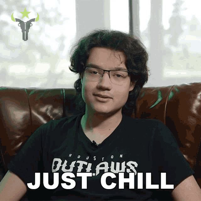 a young man wearing a houston outlaws shirt sits on a leather couch