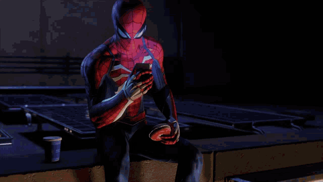 a man in a spiderman costume is sitting on a ledge looking at his cell phone