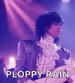 prince is playing a guitar on stage in a purple suit and white shirt .