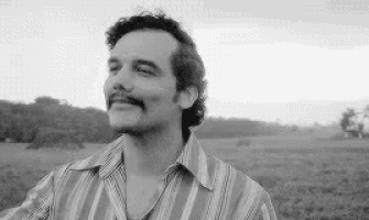 a black and white photo of a man with a mustache in a striped shirt standing in a field .