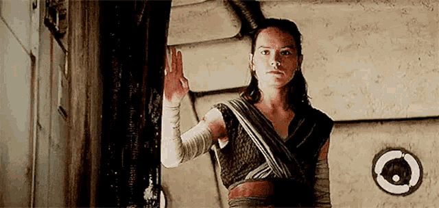 a woman is standing next to a wall with her hand on it and waving .