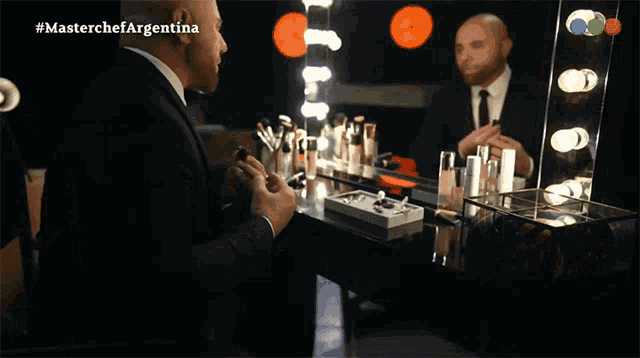 a man in a suit is applying makeup in front of a mirror with #masterchefargentina written on it