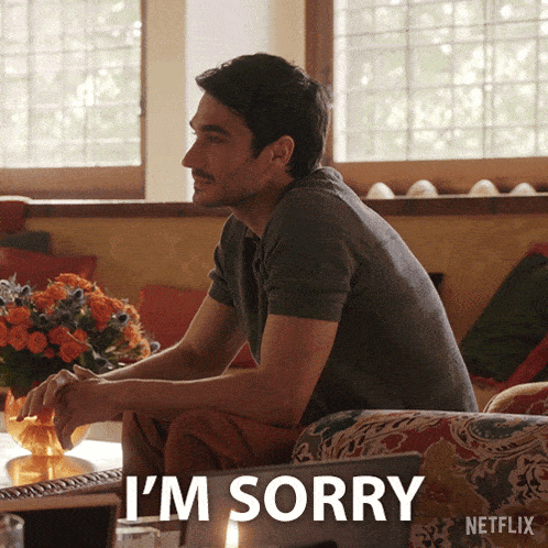 a man sits on a couch with the words " i 'm sorry " behind him