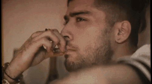 a man with a beard is smoking a cigarette in a bedroom .