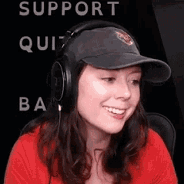 a woman wearing a hat and headphones is smiling in front of a sign .