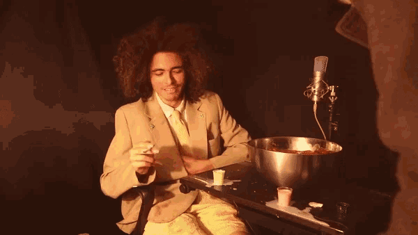 a man in a suit sits at a table with a bowl of blood