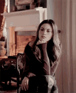 a woman sitting in a chair with her hand on her chin in front of a fireplace