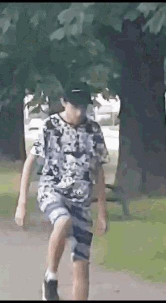 a young boy wearing a hat and shorts is walking down a path in a park