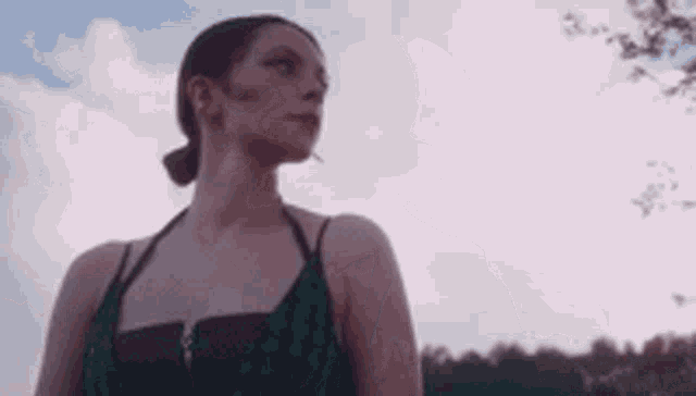 a woman in a green dress is standing in front of a cloudy sky looking up .