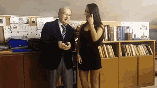 a man and a woman are standing next to each other in front of a bookshelf