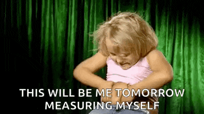 a little girl is measuring her waist with a green curtain in the background .
