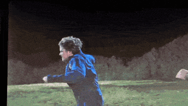 a man in a blue jacket is running on a grassy field at night .