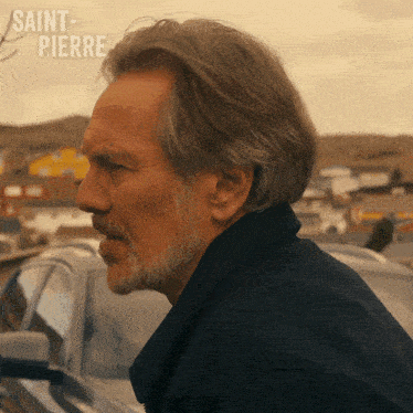 a man with a beard is standing in front of a car with saint-pierre written on the bottom