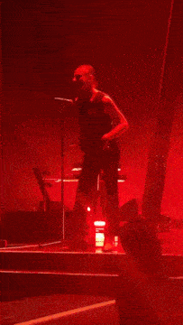 a man singing into a microphone on a stage with red lights