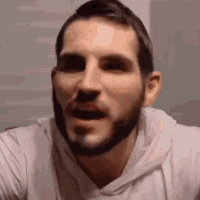 a man with a beard is wearing a white hoodie and making a face .