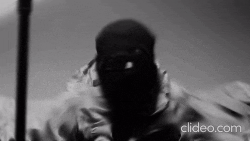 a black and white photo of a man with a mask on his face holding a cane .
