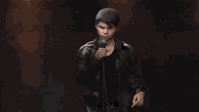 a man in a leather jacket is singing into a microphone in a dark room