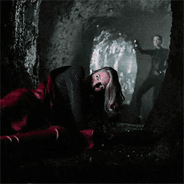 a woman is laying on the ground in a dark cave with a red light coming out of the ceiling .