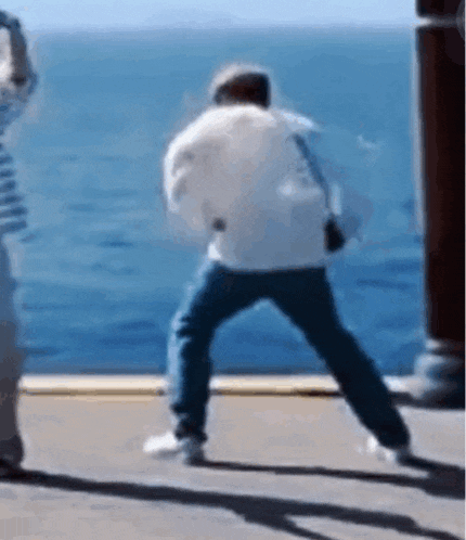a man is standing on a sidewalk in front of the ocean .