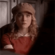 a woman wearing a hat and a red dress is looking at another woman .