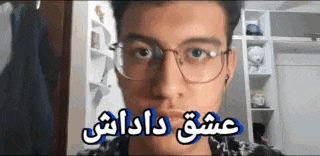 a young man wearing glasses and ear buds is looking at the camera with a foreign language on his face .