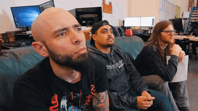three men are sitting on a couch and one has a shirt that says supreme