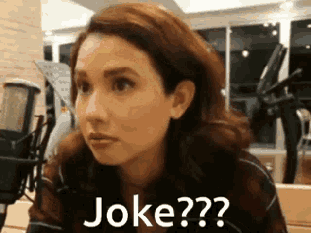 a woman sitting in front of a microphone with the words joke written on her face .