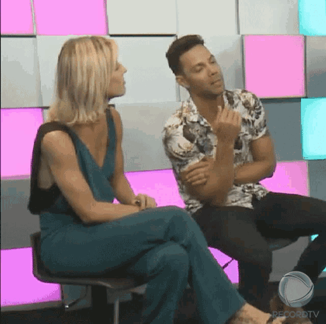 a man and a woman are sitting next to each other in front of a wall .