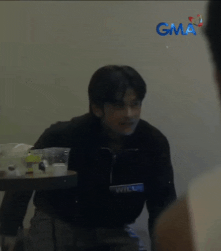 a blurry picture of a man standing in front of a table with a gma logo on the wall behind him